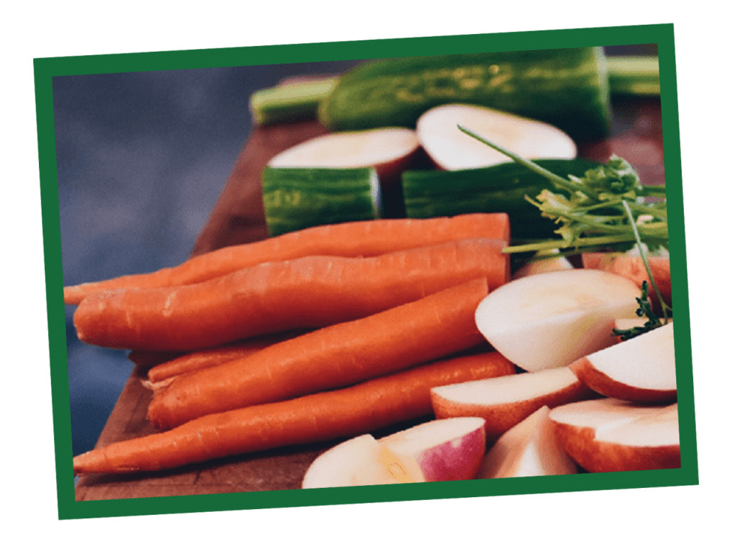 Fresh carrots with green tops on a wooden cutting board.