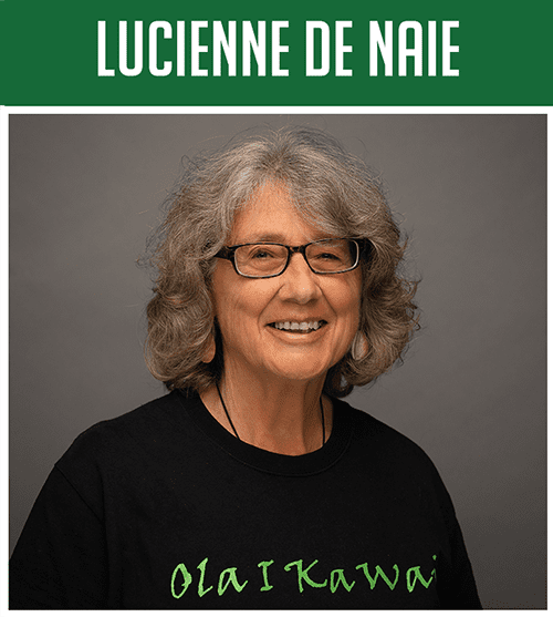 lucienne3 Portrait of an older woman with gray curly hair and glasses, smiling, wearing a black shirt against a gray backdrop.