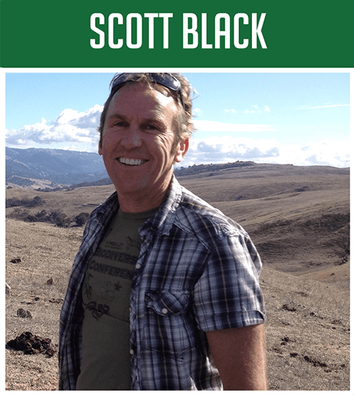 scott3 Smiling man in a plaid shirt standing in a dry, hilly landscape with a green banner reading SCOTT BLACK above him.