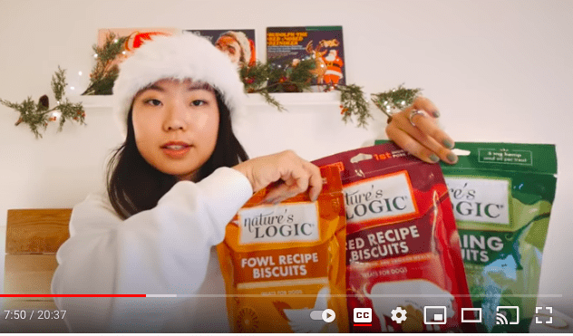 nl-social A young woman wearing a Santa hat points at colorful snack bags on a table in a Christmas setting.