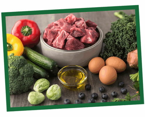 Assorted fresh ingredients on a cutting board: red bell pepper, bowl of chopped onions, garlic, Brussels sprouts, a bottle of olive oil, and eggs.