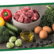 Assorted fresh ingredients on a cutting board: red bell pepper, bowl of chopped onions, garlic, Brussels sprouts, a bottle of olive oil, and eggs.